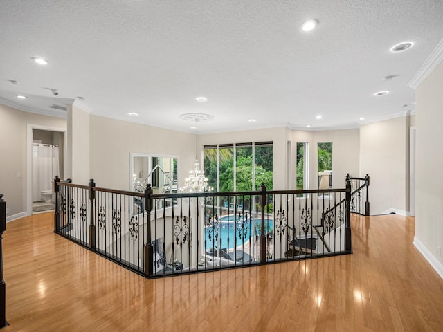 hall with a textured ceiling, hardwood / wood-style flooring, an inviting chandelier, and crown molding