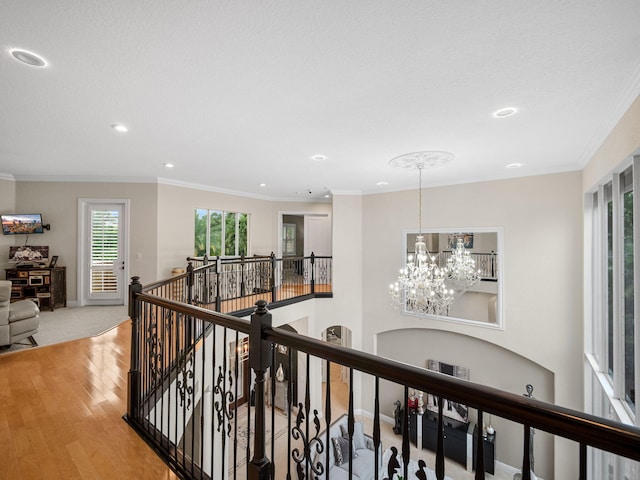 hallway with hardwood / wood-style flooring, crown molding, and a notable chandelier