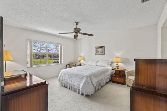 bedroom with a textured ceiling, light colored carpet, and ceiling fan