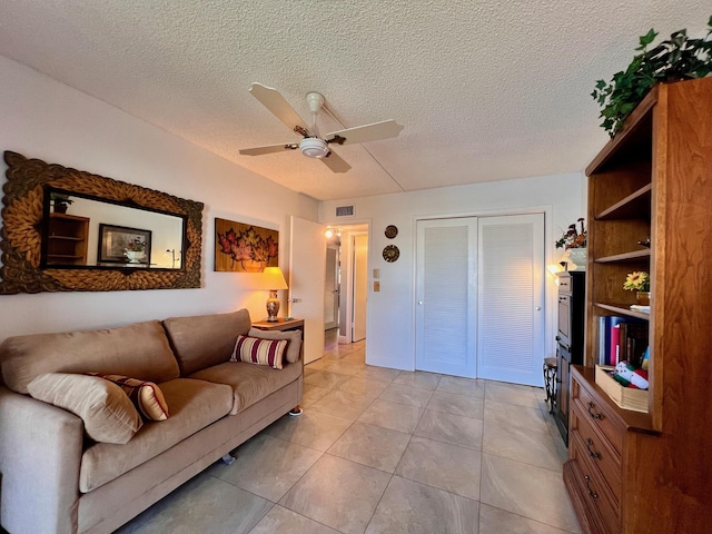 living room featuring ceiling fan, light tile patterned flooring, and a textured ceiling