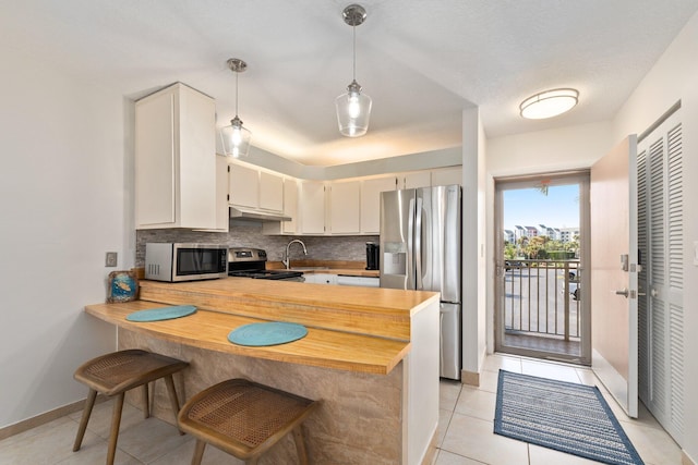 kitchen with pendant lighting, cream cabinets, tasteful backsplash, kitchen peninsula, and stainless steel appliances