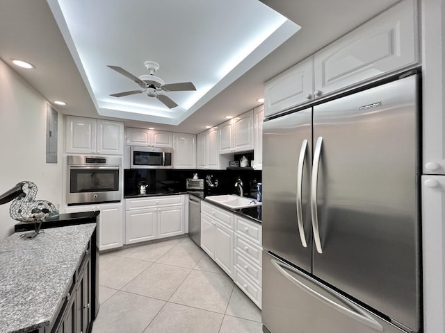 kitchen with white cabinets, sink, light tile patterned floors, a tray ceiling, and stainless steel appliances