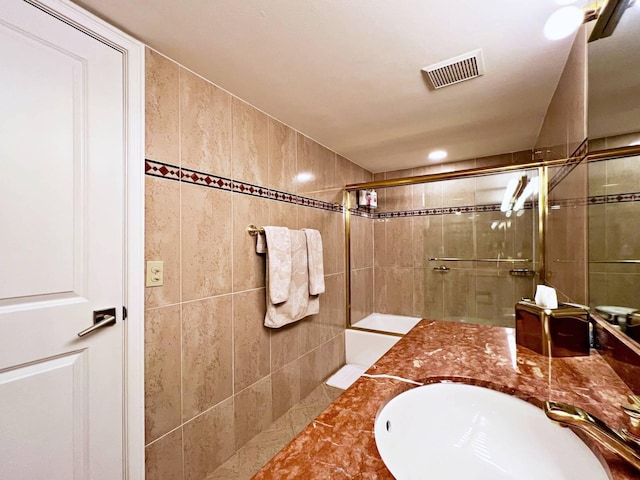 bathroom with a shower with door, tile walls, and sink