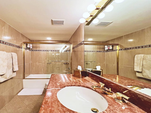 bathroom with tile patterned floors, vanity, enclosed tub / shower combo, and tile walls