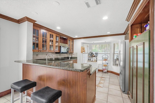 kitchen with stainless steel refrigerator, a kitchen breakfast bar, kitchen peninsula, crown molding, and dark stone countertops