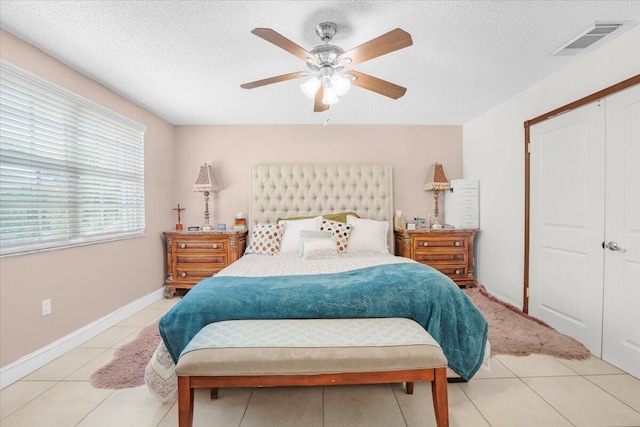 tiled bedroom with ceiling fan, a textured ceiling, and a closet