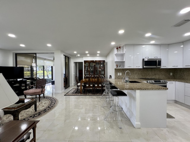 kitchen with dark stone counters, white cabinets, sink, kitchen peninsula, and stainless steel appliances