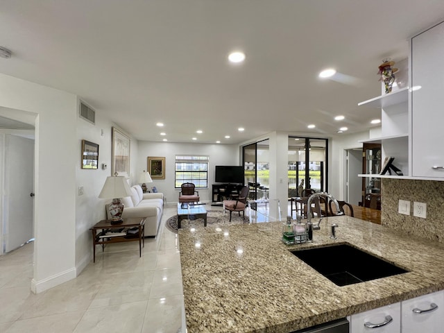 kitchen with light stone countertops, sink, tasteful backsplash, light tile patterned flooring, and white cabinets