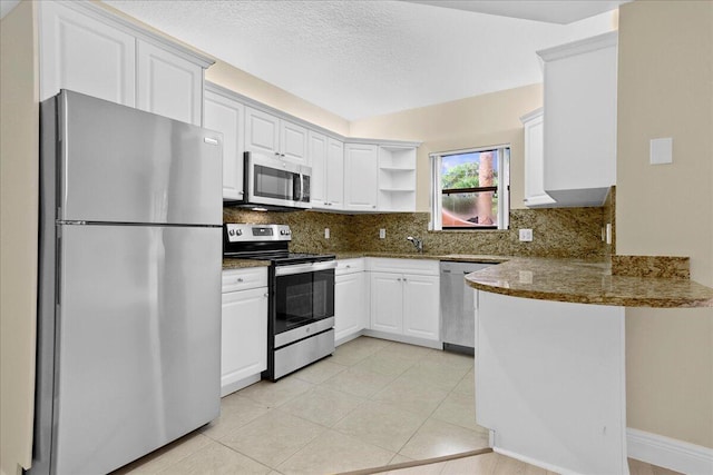 kitchen featuring white cabinets, dark stone countertops, tasteful backsplash, kitchen peninsula, and stainless steel appliances