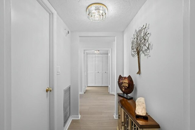 hall with a chandelier, light hardwood / wood-style floors, and a textured ceiling