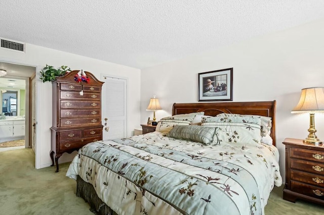 bedroom with light carpet, ensuite bathroom, and a textured ceiling