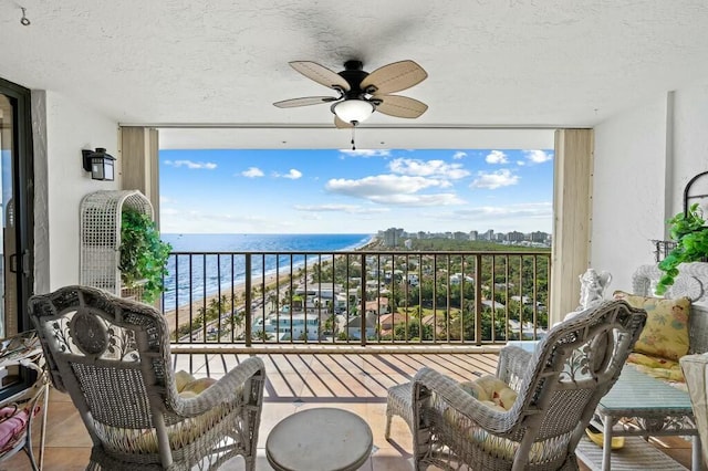 balcony with a view of the beach, a water view, and ceiling fan