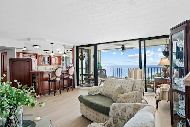 living room featuring light wood-type flooring, a water view, expansive windows, and ceiling fan