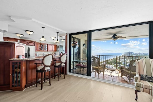 interior space featuring pendant lighting, stainless steel refrigerator with ice dispenser, ceiling fan, light wood-type flooring, and light stone counters