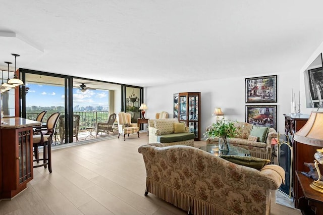 living room with ceiling fan, light hardwood / wood-style floors, and a wall of windows