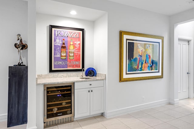 bar with light tile patterned flooring, light stone countertops, white cabinetry, and beverage cooler