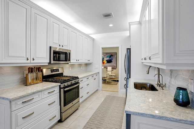 kitchen with light stone counters, stainless steel appliances, sink, light tile patterned floors, and white cabinetry