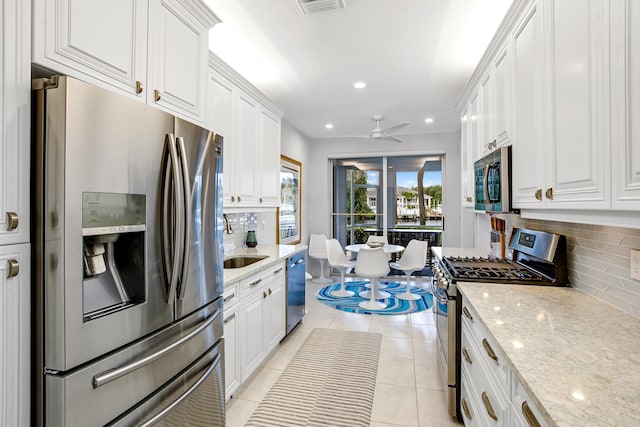 kitchen featuring tasteful backsplash, light stone counters, stainless steel appliances, ceiling fan, and white cabinets