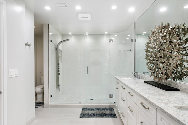 bathroom featuring tile patterned flooring, vanity, a shower with shower door, and toilet