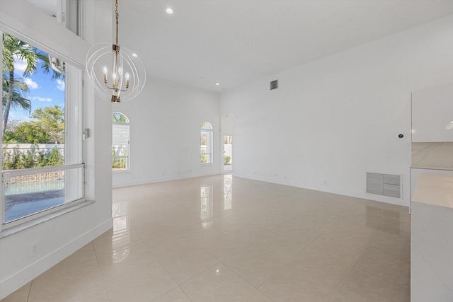 spare room with light tile patterned floors, a high ceiling, and an inviting chandelier