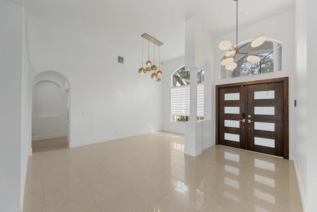 tiled foyer entrance featuring a notable chandelier, a healthy amount of sunlight, a high ceiling, and french doors