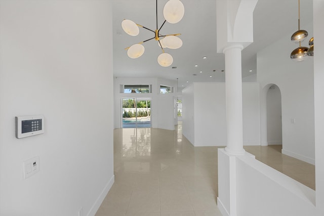 hall with light tile patterned floors, an inviting chandelier, and ornate columns