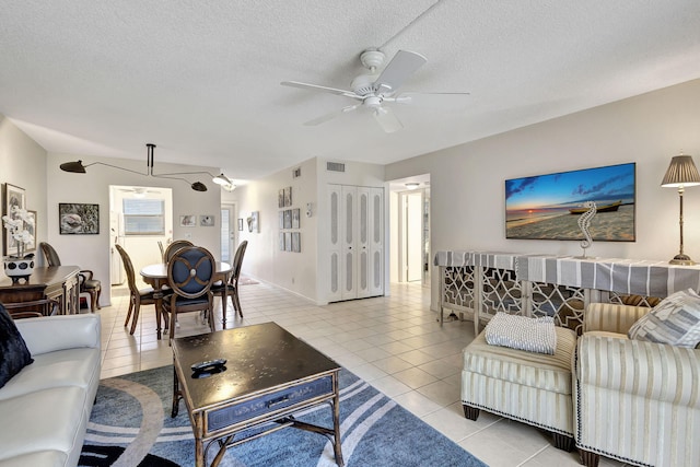 living room with ceiling fan, light tile patterned flooring, and a textured ceiling