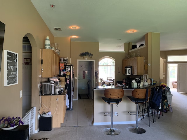 kitchen with kitchen peninsula, stainless steel fridge, a breakfast bar area, and light tile patterned flooring