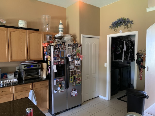 kitchen with stainless steel fridge with ice dispenser, light tile patterned floors, washer and clothes dryer, and dark stone countertops