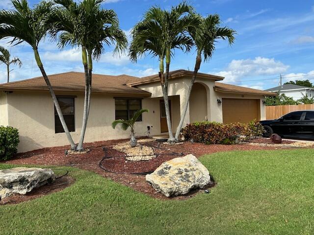 view of front facade with a garage, fence, a front lawn, and stucco siding