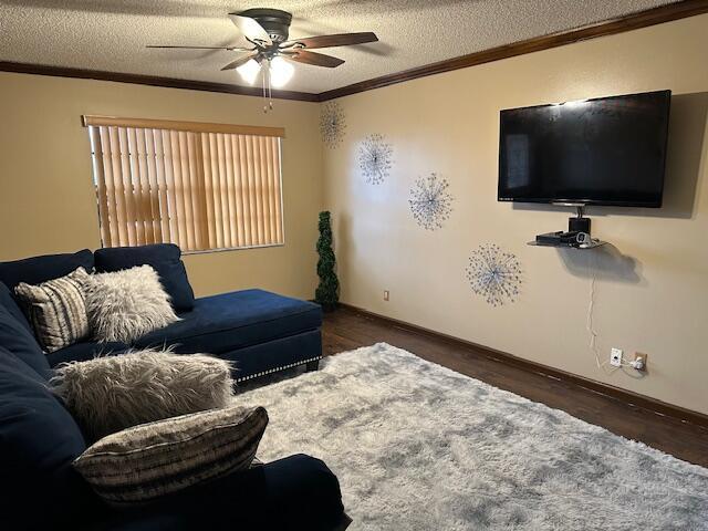 living room with crown molding, dark hardwood / wood-style flooring, ceiling fan, and a textured ceiling