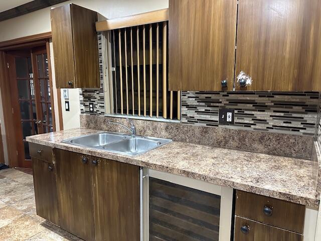 kitchen with backsplash, light stone counters, sink, and wine cooler