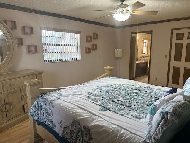 bedroom featuring ceiling fan, ensuite bathroom, a textured ceiling, crown molding, and light wood-type flooring