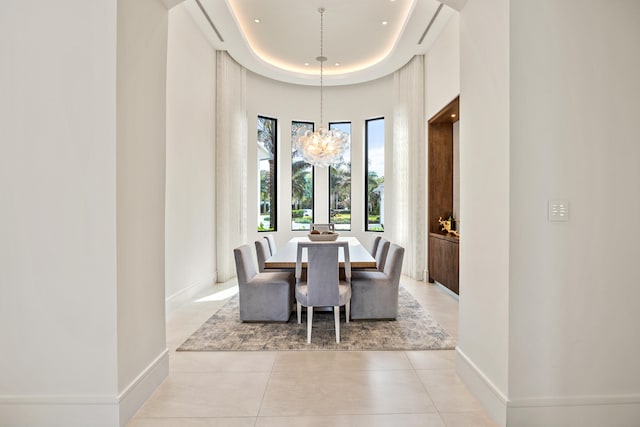 tiled dining space featuring a raised ceiling, a chandelier, and a high ceiling