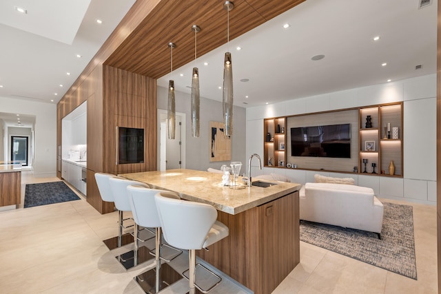 kitchen featuring sink, light stone counters, a kitchen bar, decorative light fixtures, and a large island with sink