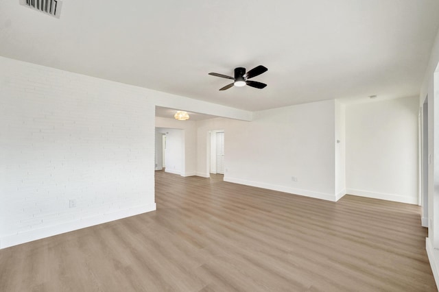 empty room featuring hardwood / wood-style flooring, ceiling fan, and brick wall