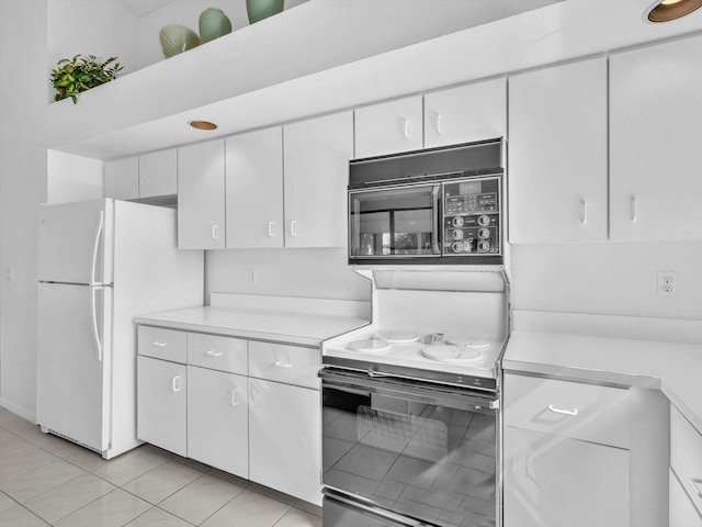 kitchen with light tile patterned floors, white fridge, white cabinetry, and range with electric stovetop