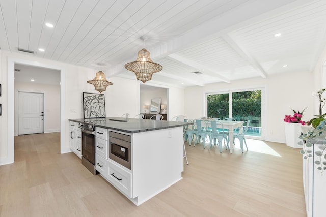 kitchen featuring beam ceiling, white cabinetry, a kitchen breakfast bar, light hardwood / wood-style flooring, and a center island with sink