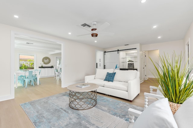 living room with ceiling fan, a barn door, and light wood-type flooring