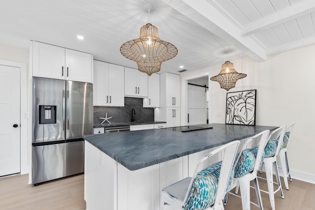 kitchen with appliances with stainless steel finishes, pendant lighting, a barn door, beam ceiling, and white cabinets