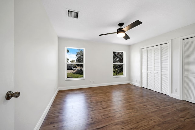 unfurnished bedroom featuring dark wood-type flooring, ceiling fan, a textured ceiling, and two closets