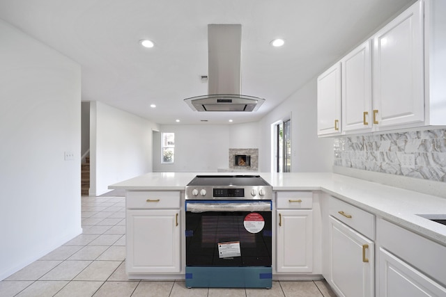 kitchen with stainless steel range with electric stovetop, white cabinetry, island exhaust hood, light tile patterned flooring, and kitchen peninsula