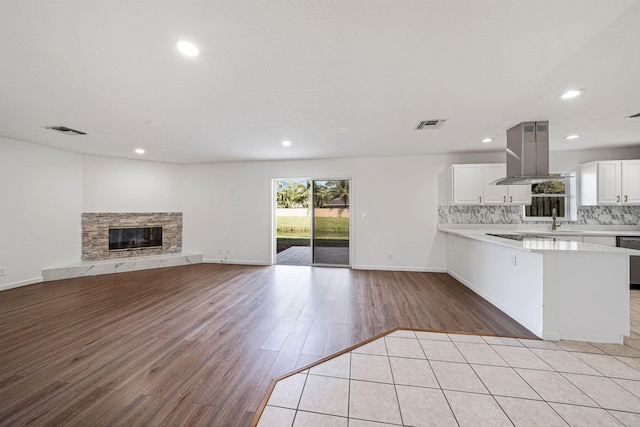 kitchen featuring light hardwood / wood-style flooring, backsplash, white cabinets, a stone fireplace, and kitchen peninsula