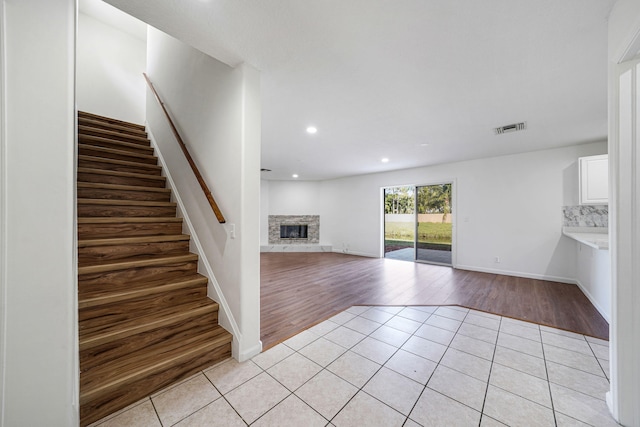 unfurnished living room with light tile patterned flooring and a stone fireplace