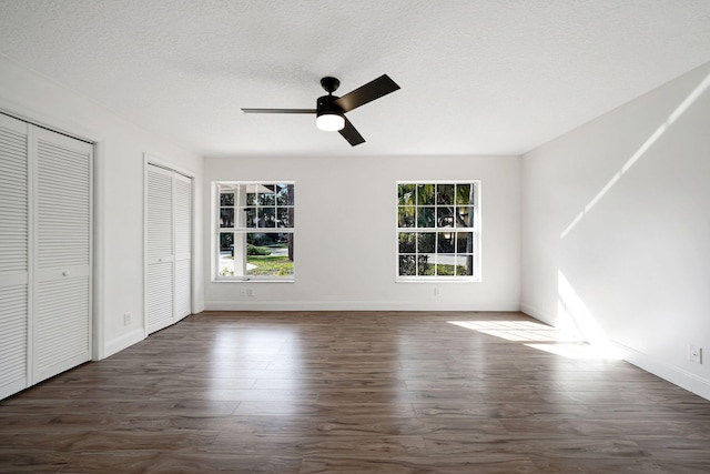 unfurnished bedroom featuring dark hardwood / wood-style flooring, two closets, a textured ceiling, and ceiling fan