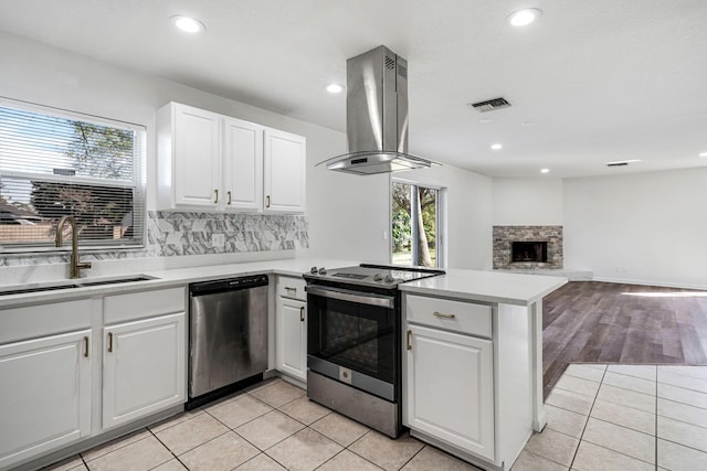 kitchen with sink, stainless steel appliances, white cabinets, island exhaust hood, and kitchen peninsula