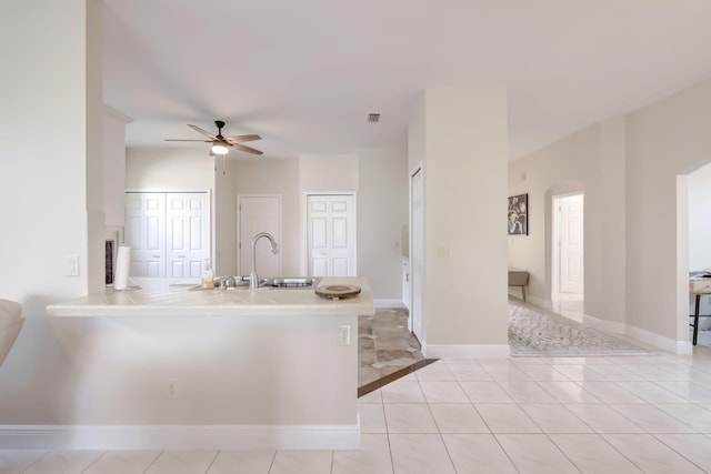 kitchen with a peninsula, baseboards, tile counters, and a sink