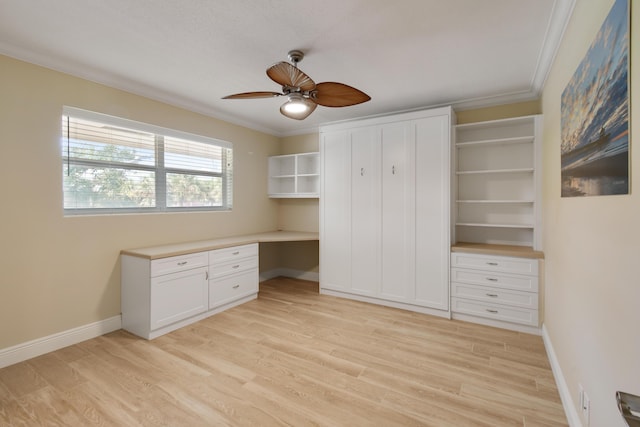 unfurnished office featuring ceiling fan, built in desk, ornamental molding, and light hardwood / wood-style flooring