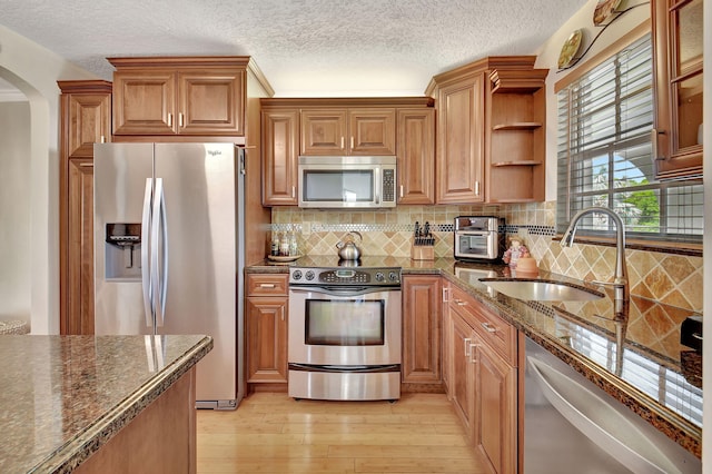 kitchen featuring sink, appliances with stainless steel finishes, dark stone countertops, decorative backsplash, and light wood-type flooring