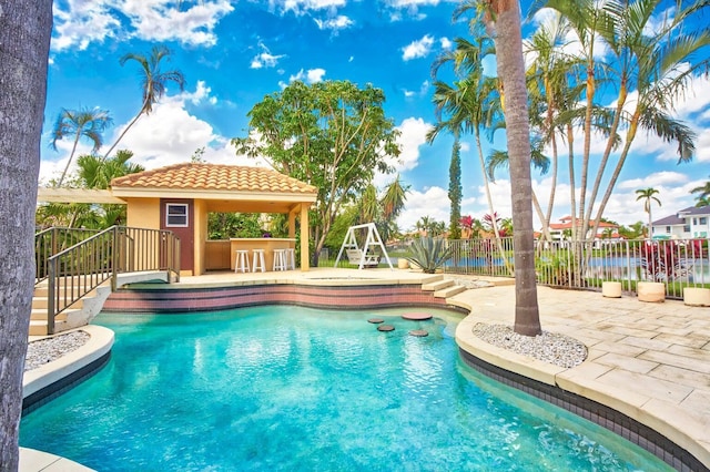 view of pool featuring a water view, an outdoor bar, and a patio